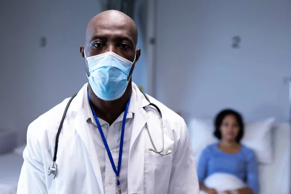 顔のマスクを着て病院でアフリカ系アメリカ人男性医師の肖像画 ベッドで女性患者 コロナウイルス感染症の治療に従事する医療従事者は — ストック写真