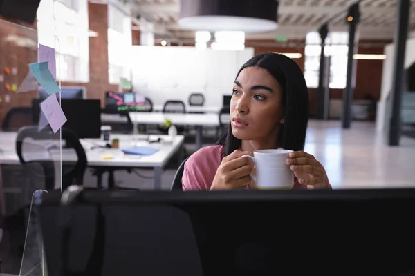 コンピュータの前にオフィスに座ってコーヒーを飲んでいる混合人種の実業家 独立した創造的なデザインビジネス — ストック写真