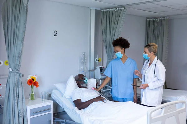 Duas Médicas Diferentes Usando Máscaras Lado Paciente Masculino Quarto Hospital — Fotografia de Stock