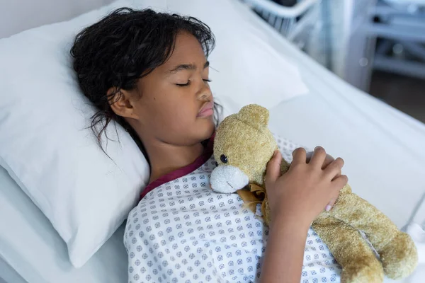 病院病棟のベッドで寝そべっているテディベアを抱えている複雑な人種の病気の少女 医療サービス — ストック写真