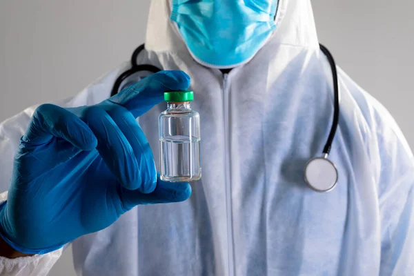 保護服を着た保健従事者のミッドセクションでは Covid 19ワクチンボトルを保持 コロナウイルス発生防止のための予防接種 — ストック写真