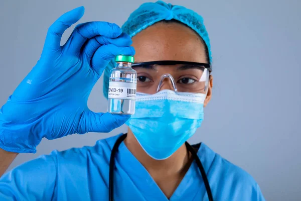 灰色の背景に対してCovid 19ワクチンボトルを保持している女性外科医の閉鎖 コロナウイルス発生防止のための予防接種 — ストック写真