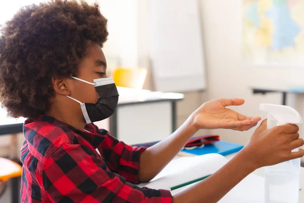 教室の机に座って手を消毒顔マスクのアフリカ系アメリカ人の少年 コロナウイルス感染症の小児期と小学校教育 Covid19パンデミック — ストック写真