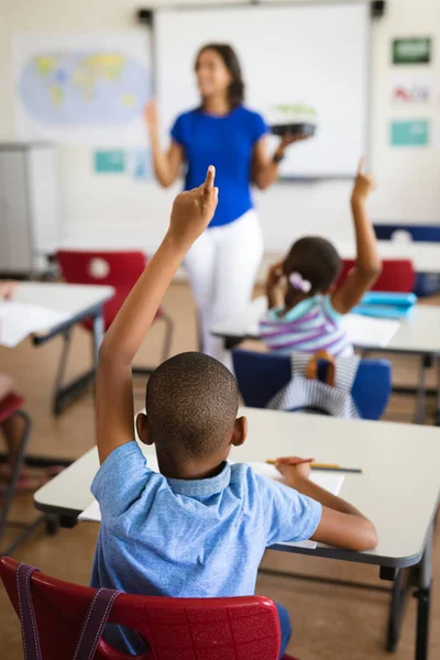アフリカ系アメリカ人の少年が学校の教室で机の上に座りながら手を上げている姿を見ることができる 学校や教育の概念 — ストック写真