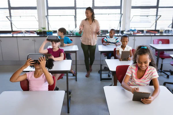アフリカ系アメリカ人の女性教師が生徒に学校の授業で電子機器を使うように教えている 学校や教育の概念 — ストック写真