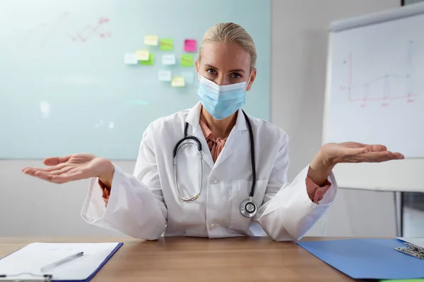 Kaukasische Ärztin Mit Gesichtsmaske Sitzt Schreibtisch Büro Und Gestikuliert Während — Stockfoto