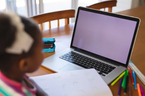 非洲裔美国女孩坐在餐桌前 手里拿着笔和书 使用笔记本电脑 在屏幕上复制空间 在线教育 家庭教育 — 图库照片