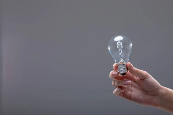 灰色の背景に隔離された電球を保持する実業家のクローズアップ ビジネス技術コミュニケーション成長の概念 — ストック写真