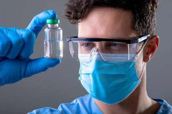 白种人男医生戴着口罩 戴着安全眼镜 手里拿着疫苗瓶 Covid期间的医疗和保健技术概念 数码合成的19个大肠病毒大流行病概念 — 图库照片