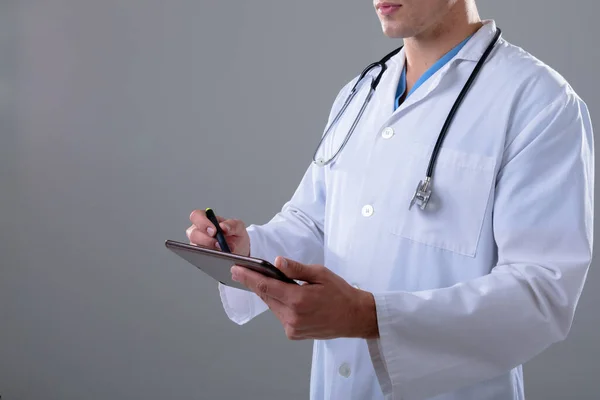 灰白質の背景に隔離されたタブレットを使用して白人男性医師の中央部 ヘルスケアサービスのコンセプトはデジタルで複合画像を生成 — ストック写真