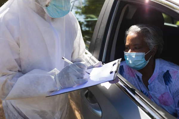 Pracownik Medyczny Garniturze Robi Notatki Rozmawiając Starszą Afroamerykanką Siedzącą Samochodzie — Zdjęcie stockowe
