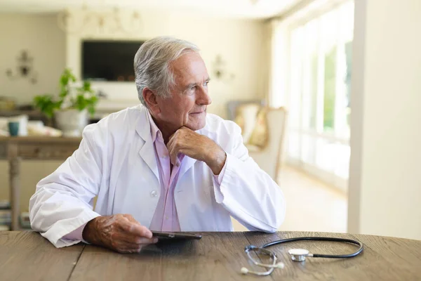 Starszy Kaukaski Lekarz Siedzący Przy Stole Przy Pomocy Tabletu Koncepcja — Zdjęcie stockowe