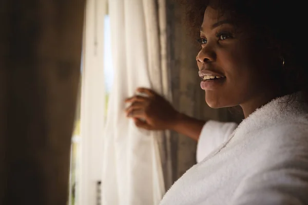Счастливая Африканская Американка Стоит Солнечного Окна Задергивая Занавески Улыбаясь Проводить — стоковое фото