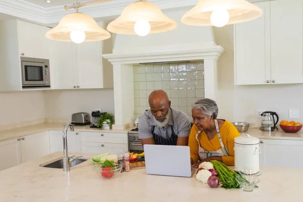シニアアフリカ系アメリカ人のカップルは ラップトップを使用してキッチンで一緒に調理します 隠遁と退職と幸せなシニアライフスタイルのコンセプト — ストック写真