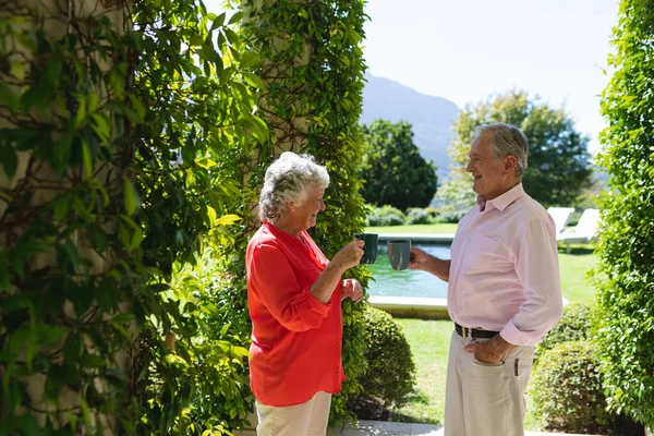 Senior Pareja Caucásica Sonriendo Sosteniendo Tazas Jardín Soleado Retiro Jubilación — Foto de Stock