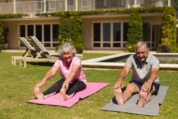 日当たりの良い庭でストレッチヨガを練習シニア白人夫婦の肖像画 定年退職と積極的なシニアライフスタイルのコンセプト — ストック写真