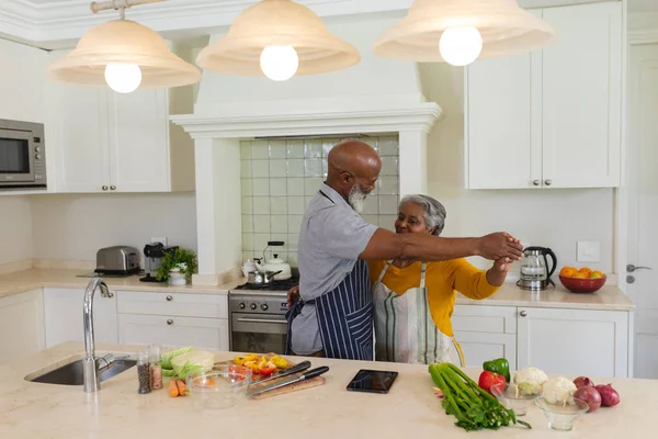 シニアアフリカ系アメリカ人のカップルがキッチンで笑顔で踊る 隠遁と退職と幸せなシニアライフスタイルのコンセプト — ストック写真