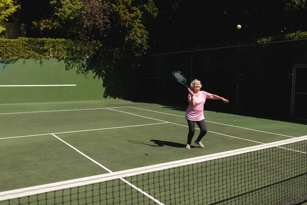 シニア白人女性がテニスラケットを持ってコートでテニスをしている 定年退職と積極的なシニアライフスタイルのコンセプト — ストック写真