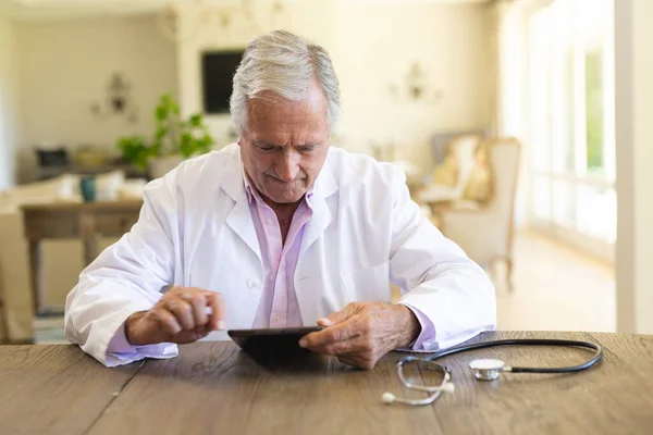 Starszy Kaukaski Lekarz Siedzący Przy Stole Przy Pomocy Tabletu Koncepcja — Zdjęcie stockowe