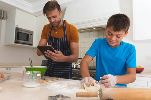 台所でタブレットや息子のベーキングや笑顔を使用して白人の父 家族で食事を共にする自由時間を楽しむ — ストック写真