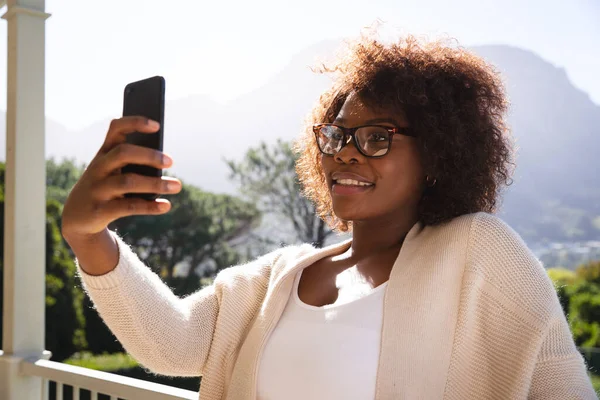 발코니에서 아프리카 미국인 여성을 웃으면서 스마트폰으로 셀카를 있습니다 집에서 시간을 — 스톡 사진