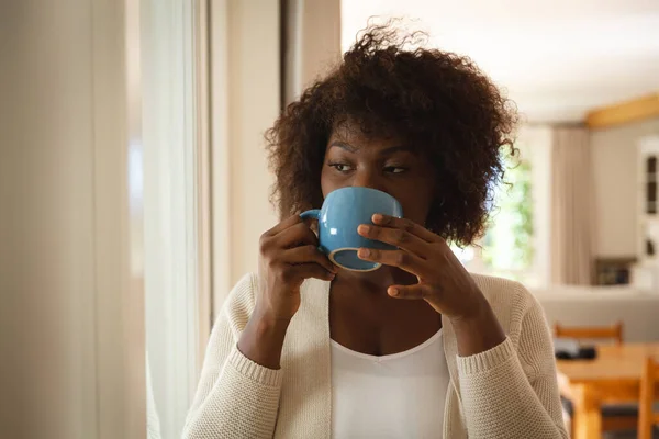 ダイニングルームでコーヒーを飲んで立っているアフリカ系アメリカ人の女性の思考 家で自由時間を過ごすと — ストック写真