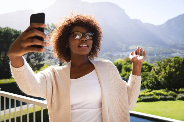 在乡间阳光灿烂的阳台上 快乐的非洲裔美国女人用智能手机进行视频通话 在家里消磨时间 — 图库照片