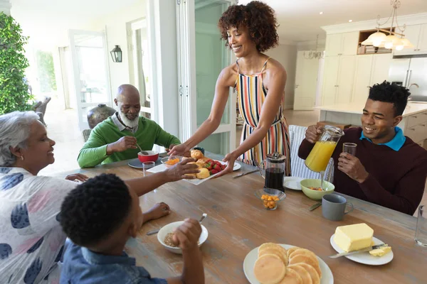 Happy african american multi generation family sitting at table during breakfast and smiling. family enjoying quality free time together.