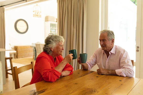 キッチンでコーヒーを飲みながらテーブルに座っている高齢者の白人夫婦 隠遁と退職と幸せなシニアライフスタイルのコンセプト — ストック写真