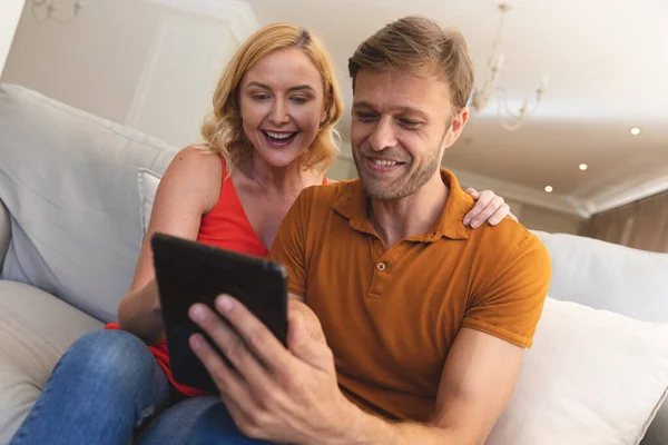 Pareja Caucásica Sentada Sofá Sonriendo Usando Tableta Casa Disfrutando Tiempo —  Fotos de Stock