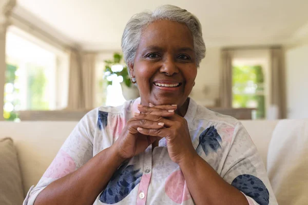 カメラを見て笑顔でソファに座っているアフリカ系アメリカ人のシニア女性の肖像画 隠遁と退職と幸せなシニアライフスタイルのコンセプト — ストック写真