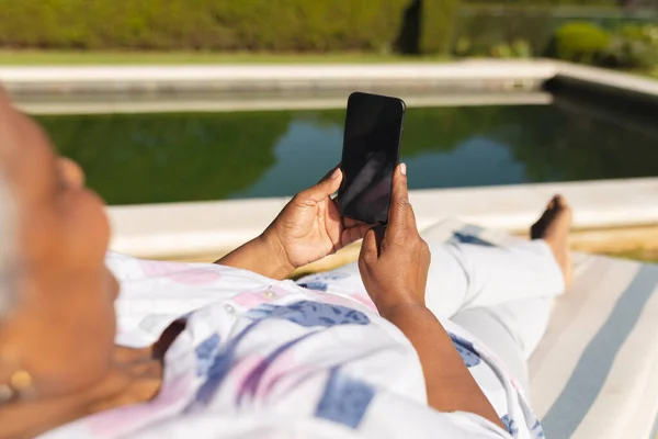 Mujer Afroamericana Mayor Usando Smartphone Tumbona Junto Piscina Jardín Soleado — Foto de Stock