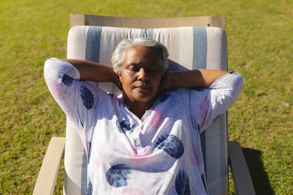 资深的非洲裔美国女人在阳光灿烂的花园里坐在躺椅上休息 退休和快乐的老年生活方式概念 — 图库照片