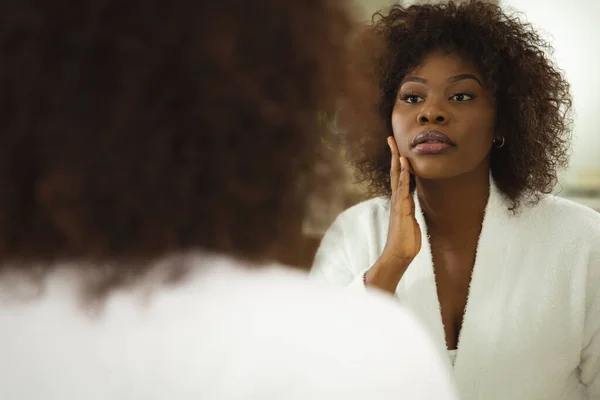 Mujer Afroamericana Baño Con Albornoz Mirando Espejo Cara Hidratante Salud —  Fotos de Stock