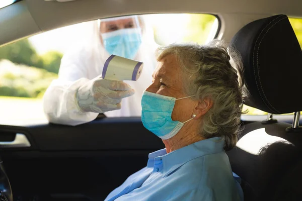 Pracownik Medyczny Garniturze Mierzący Temperaturę Starszej Białej Kobiety Siedzącej Samochodzie — Zdjęcie stockowe