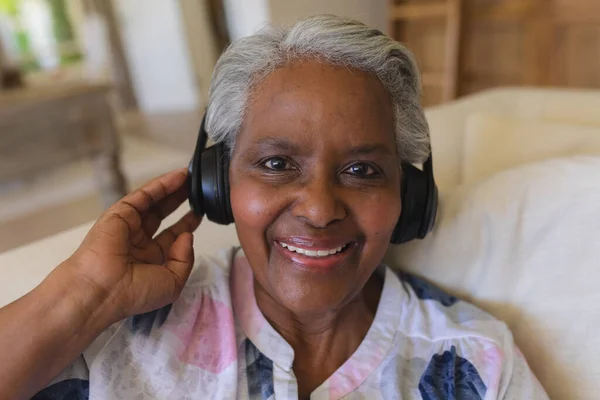坐在沙发上 头戴耳机 面带微笑的非洲裔美国老年妇女的画像 退休和快乐的老年生活方式概念 — 图库照片