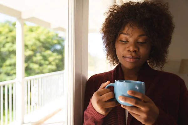 Pensativa Mujer Afroamericana Pie Junto Una Ventana Soleada Sosteniendo Una —  Fotos de Stock