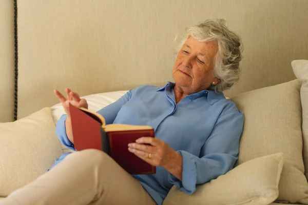 シニア白人女性がベッドに座り 寝室で本を読んでいます 隠遁と退職と幸せなシニアライフスタイルのコンセプト — ストック写真