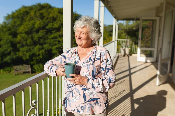 高个子高加索女人站在阳台上 举着杯子笑着 退休和快乐的老年生活方式概念 — 图库照片