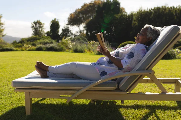 Starsza Afroamerykanka Czytająca Książkę Leżaku Słonecznym Ogrodzie Wycofanie Się Emerytura — Zdjęcie stockowe