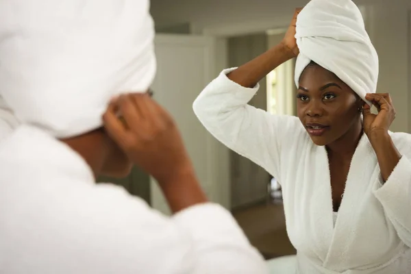 バスローブを着たバスルームでアフリカ系アメリカ人の女性は 鏡の上にタオルを頭の上に置く 健康美健康家庭で質の高い時間を過ごすこと — ストック写真