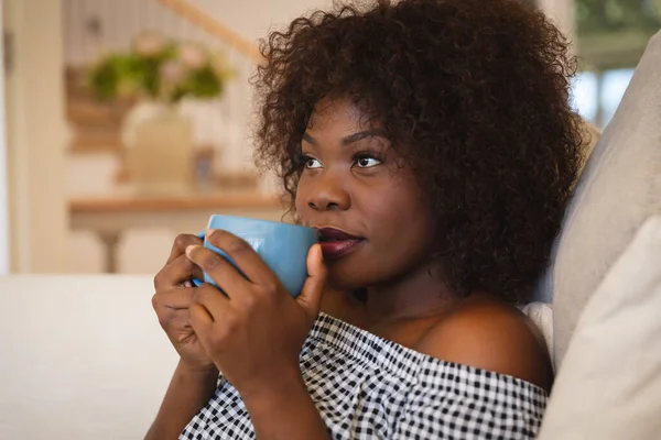 一个微笑的非洲裔美国女人坐在沙发上喝茶的画像 家庭生活方式 在家中享受闲暇时间 — 图库照片