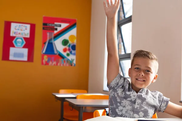 Szczęśliwy Biały Uczeń Siedzi Biurkiem Klasie Podnosząc Rękę Podczas Lekcji — Zdjęcie stockowe