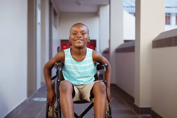 笑顔の肖像障害のあるアフリカ系アメリカ人の少年が学校の廊下に車椅子に座っている 子供の頃と小学校での教育は — ストック写真