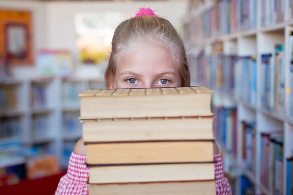在学校图书馆里带着一堆堆书的快乐的高加索女学生的画像 儿童与小学教育 — 图库照片