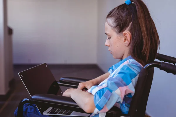 在学校走廊 残疾的高加索女学生坐在轮椅上 使用笔记本电脑 小学的儿童 技术和教育 — 图库照片