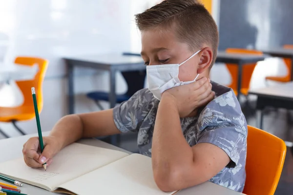 Caucasian Schoolboy Wearing Face Mask Sitting Desk Classroom Writing Book — Stock Photo, Image