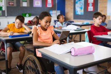 Disabled african american girl using digital tablet while sitting on wheelchair at elementary school. school and education concept clipart