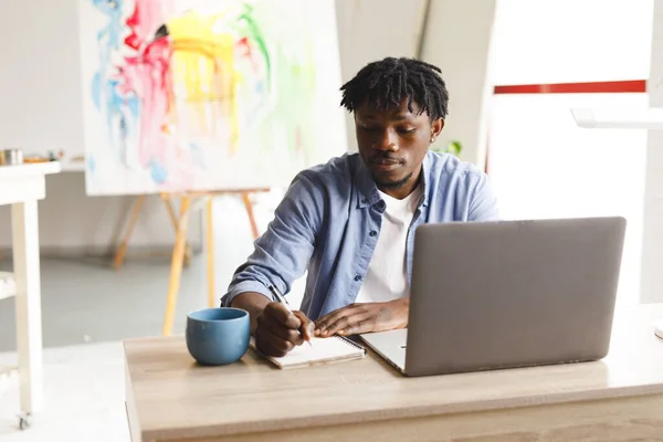 非裔美国男性画家在工作中使用笔记本电脑 并在艺术工作室做笔记 艺术家绘画工作室的创作和灵感 — 图库照片