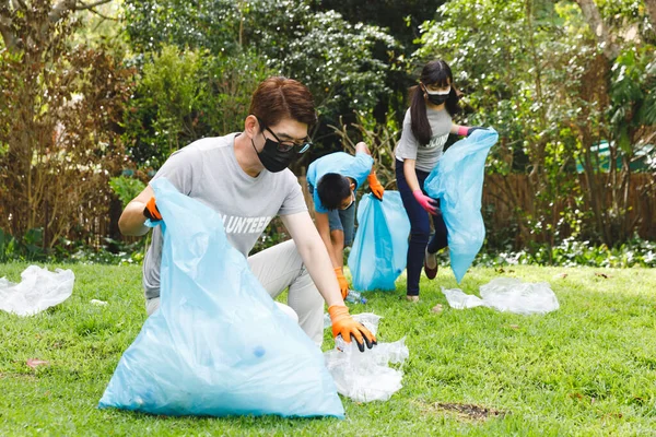 田舎ではアジア系の父親と息子と娘がゴミ袋に入った顔のマスクをしている 生態系保全ボランティアや大流行時の田舎清掃などです — ストック写真